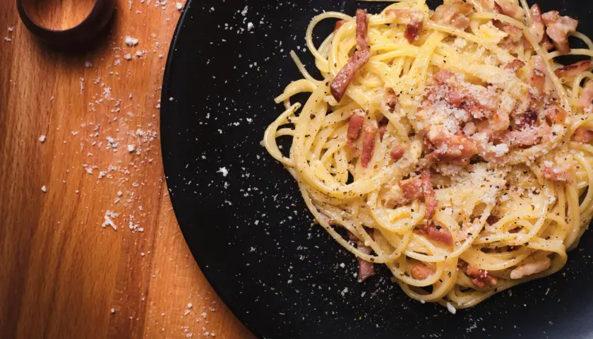 Spaghetti alla carbonara, un piatto che evoca la sua origine romana, con guanciale croccante e pecorino.