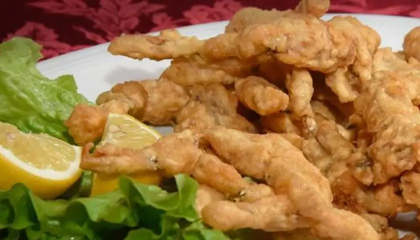 Un piatto di croccanti rane fritte, servite con spicchi di limone e foglie di lattuga fresca.