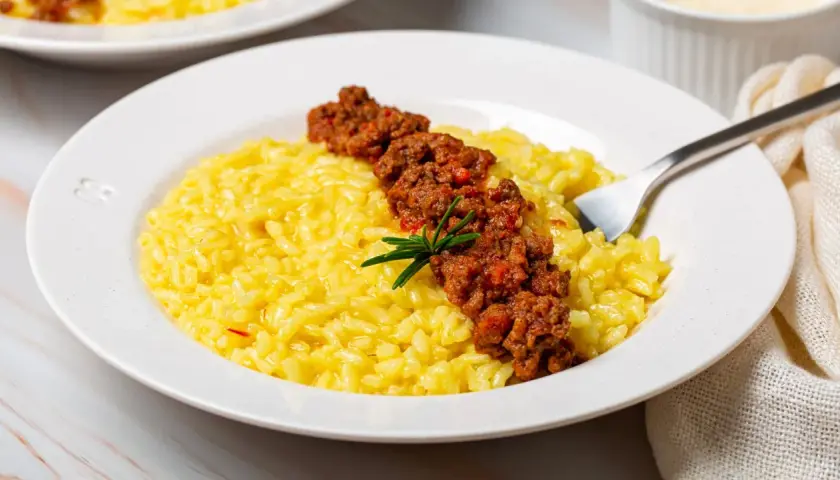 Risotto giallo cremoso con ragù di salsiccia e stracchino, guarnito con rosmarino.