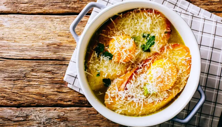 Zuppa alla pavese fumante, con pane tostato, uova e abbondante parmigiano grattugiato, servita in una ciotola bianca su un tavolo di legno rustico.