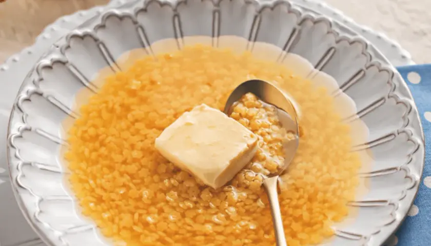 Minestrina in brodo con dado, un comfort food che scalda il cuore. Un cucchiaio d'oro raccoglie la pasta minuta e un cubetto di burro si scioglie nel brodo caldo.