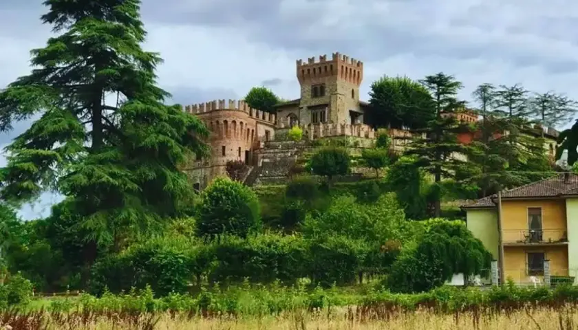 La rocca di Montalfeo, un castello medievale circondato da alberi secolari e vegetazione lussureggiante, domina la collina.