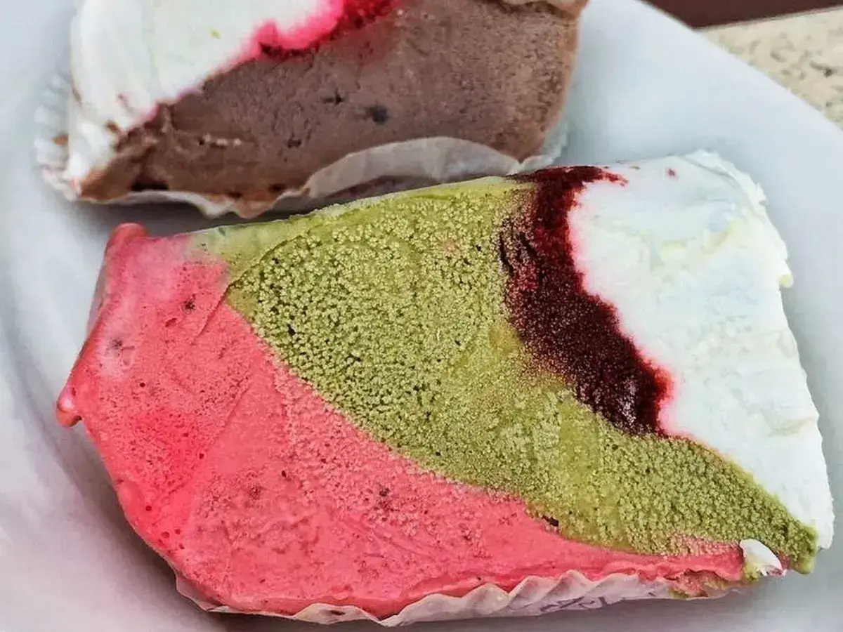 Un pezzo duro gelato a strati: rosa, verde pistacchio e bianco con striature rosse. Un altro pezzo di gelato al cioccolato e bianco è sullo sfondo.