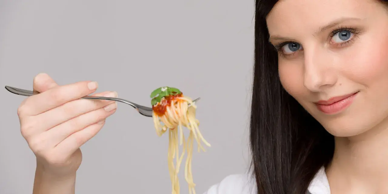 Donna con forchettata di spaghetti al pomodoro, un piatto che sembra quasi un'opera d'arte con i suoi formati di pasta strani e invitanti.