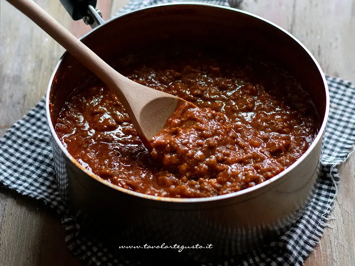 Un pentolone pieno di ragù, pronto per condire gli spaghetti. Un cucchiaio di legno mescola la salsa.