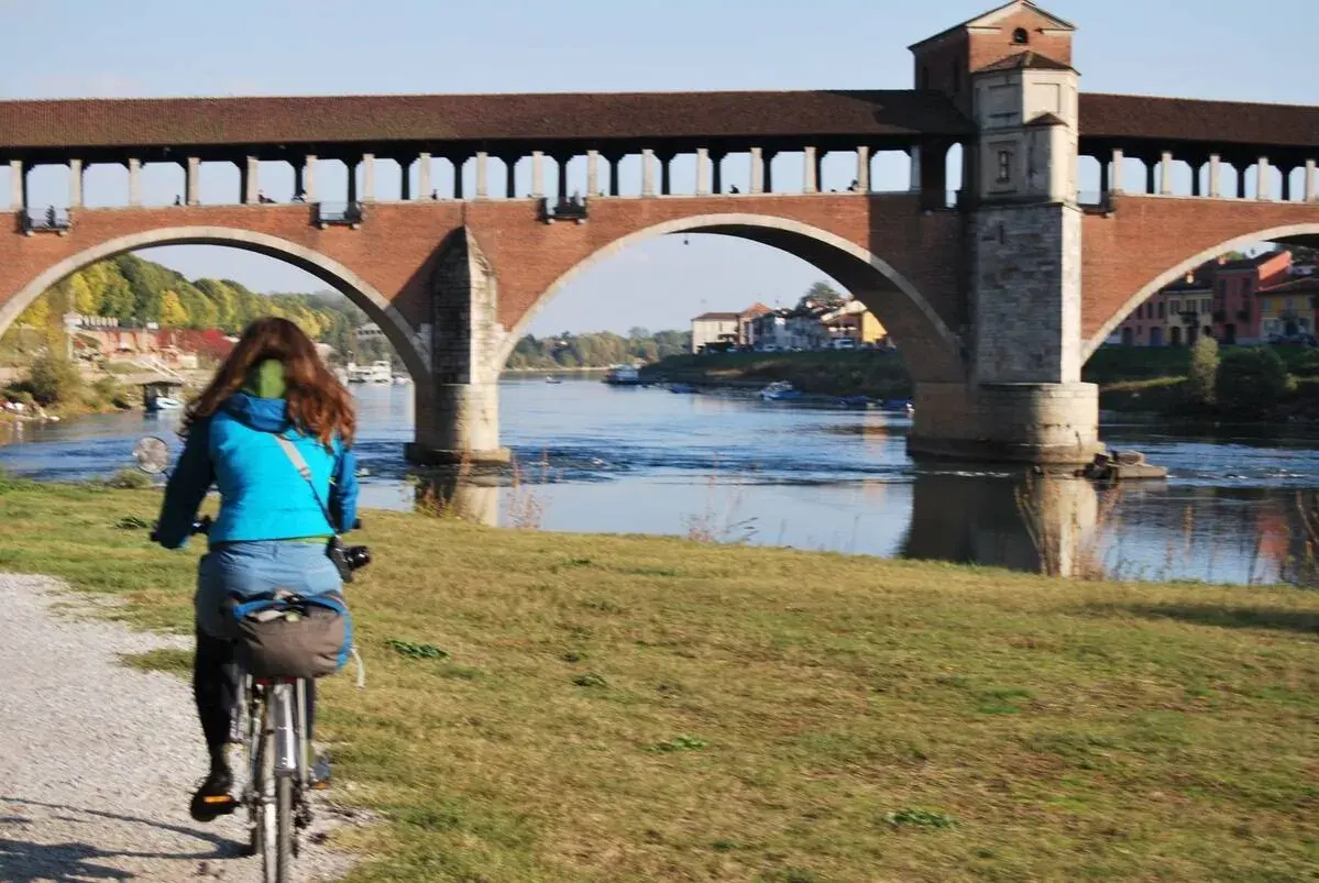 Ciclista sulla ciclabile Milano Pavia, con il Ponte Coperto di Pavia sullo sfondo.