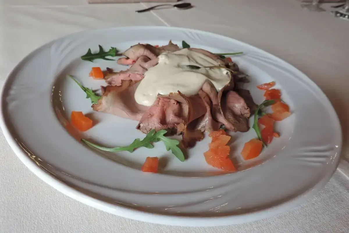 Vitello tonnato, un classico con origini piemontesi, servito su un piatto bianco con pomodorini e rucola.