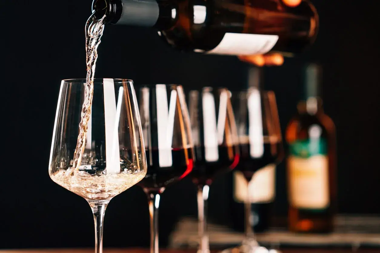 Versando vino bianco in un calice, con altri calici pieni di un intenso rosso rubino sullo sfondo.