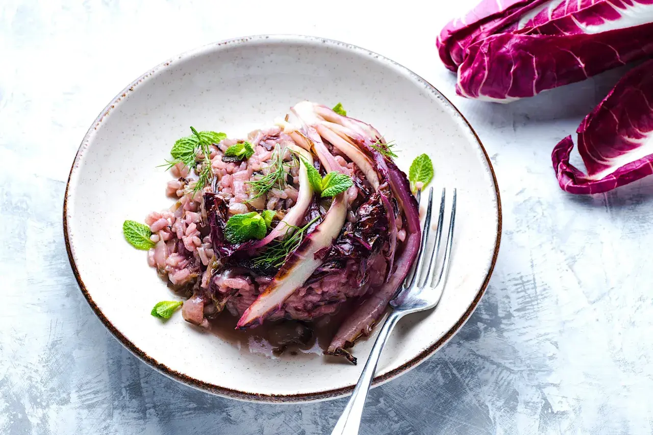 Un cremoso risotto al radicchio, guarnito con foglie di menta fresca e aneto, pronto per essere gustato.