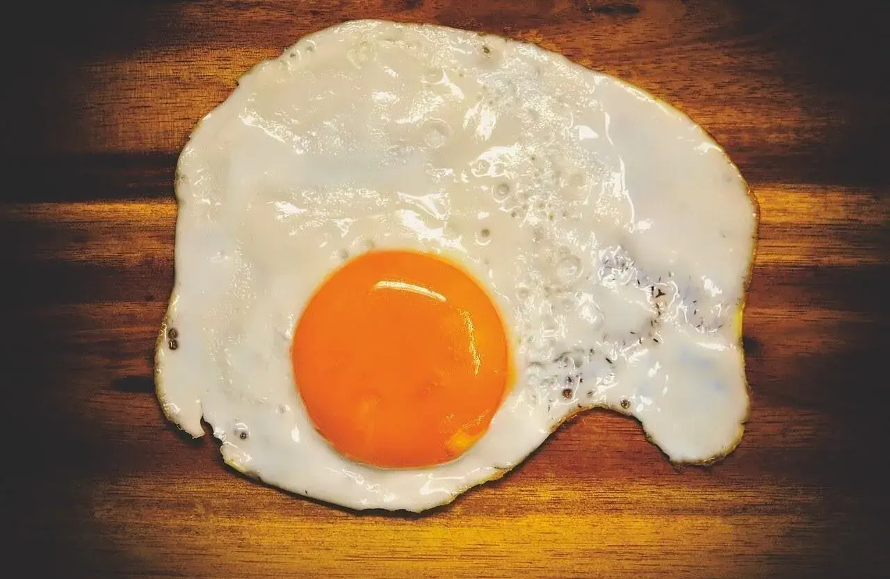 Un uovo in cereghin, cotto alla perfezione, con un tuorlo arancione brillante su un tagliere di legno scuro.