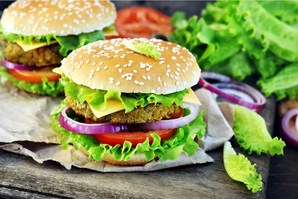 Hamburger vegetali ricetta: due succulenti hamburger con panino ai semi di sesamo, insalata croccante, pomodoro, cipolla rossa e formaggio.