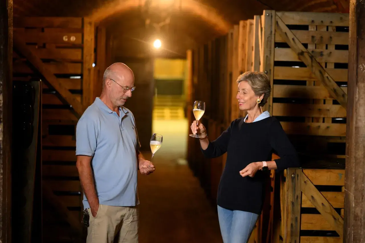 Coppia degusta vino in cantina, tra casse di legno. Il vino, affinato sur lie, brilla nei calici.