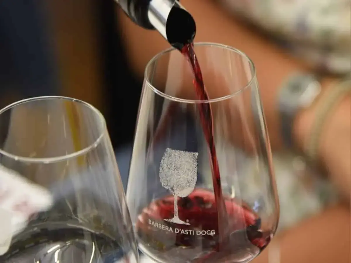 Versando il vino rosso in un bicchiere con inciso "Barbera d'Asti DOCG". Un'esperienza per gustare la barbera migliore.