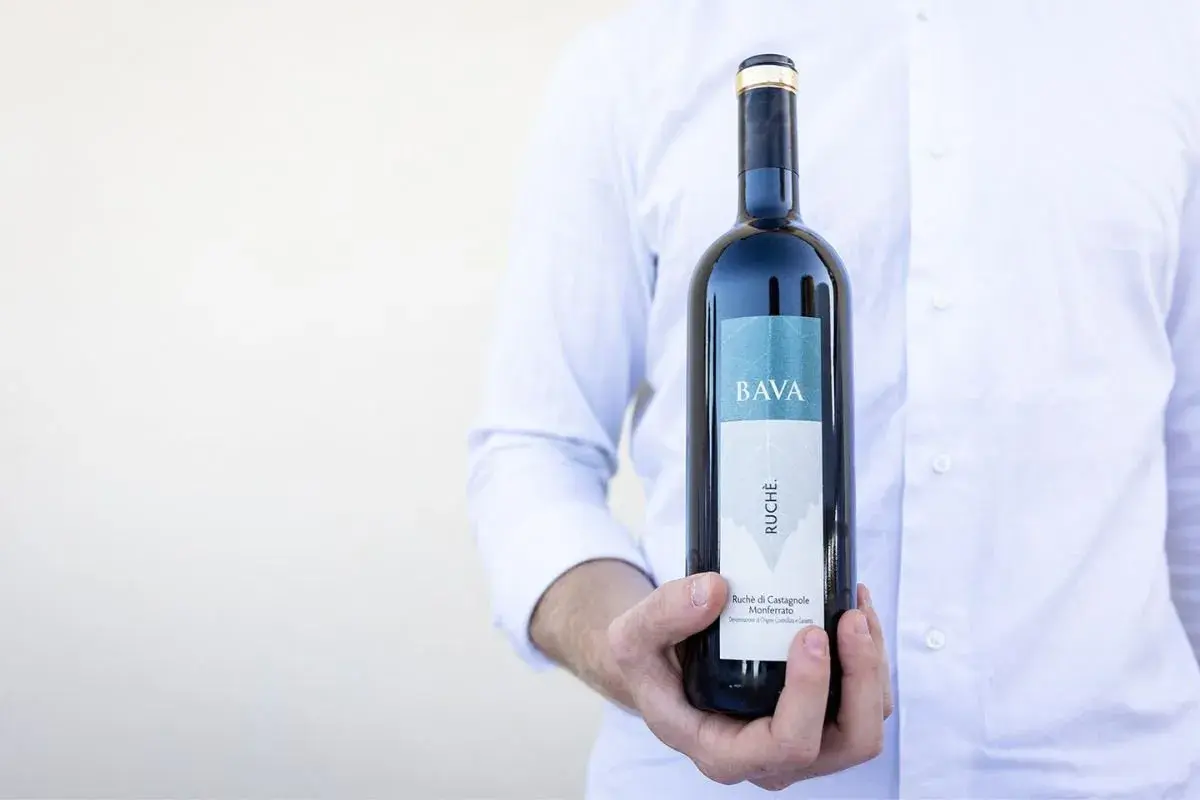 Uomo in camicia bianca tiene una bottiglia di vino Ruche di Castagnole Monferrato BAVA.