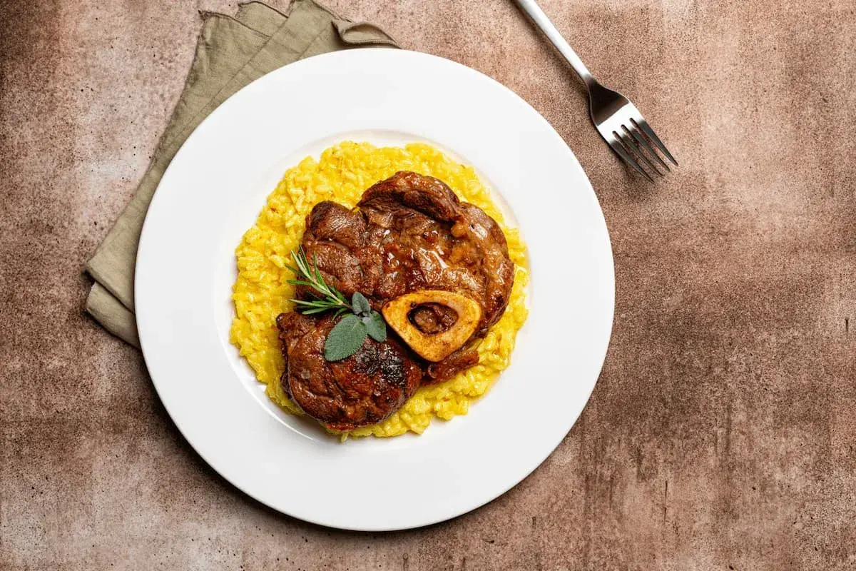 Ossobuco con risotto alla milanese, un classico dei piatti tipici Lombardia, guarnito con rosmarino e salvia.