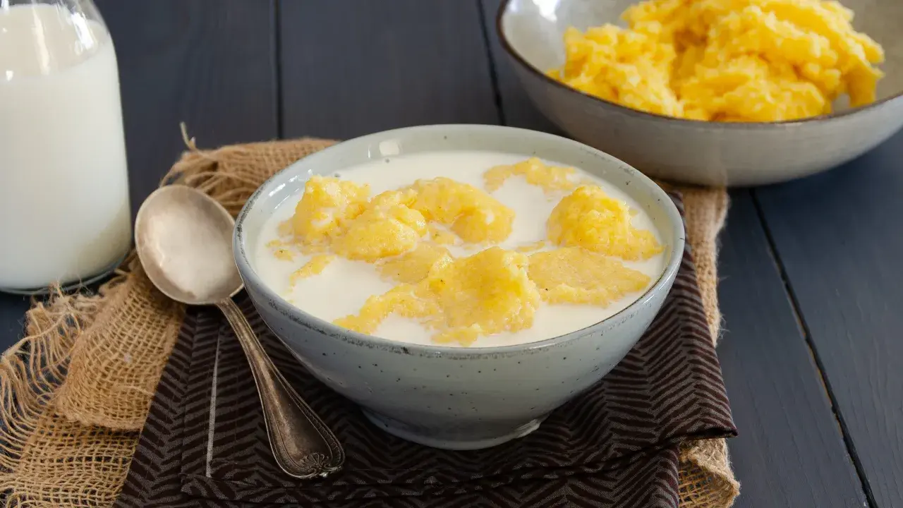 Una ciotola di polenta e latte, un piatto confortante. Accanto, una bottiglia di latte e un cucchiaio d'argento.