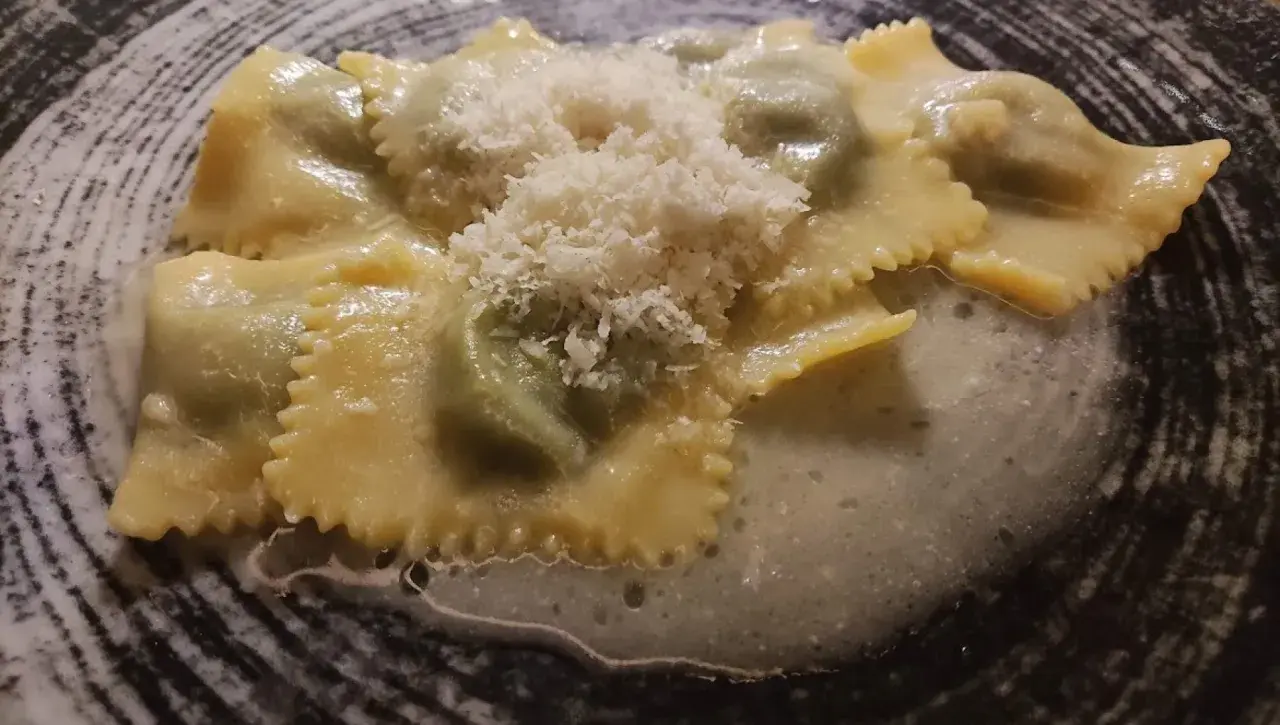 Ravioli italiani ripieni, conditi con una salsa cremosa e spolverati di parmigiano grattugiato, serviti in un piatto scuro.