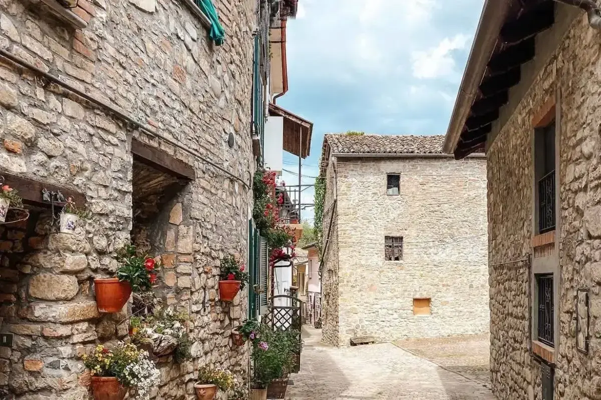 Un vicolo tra antichi borghi in provincia di Pavia, con case in pietra e vasi di fiori colorati che adornano i muri.