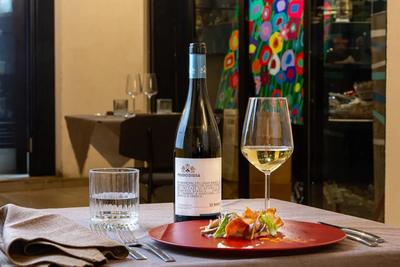 Un bicchiere di vino bianco Catarratto, con le sue caratteristiche freschezza e note agrumate, accompagna un piatto gourmet.