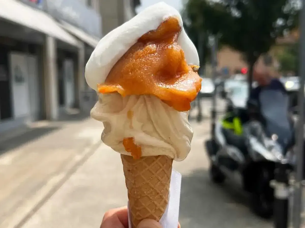 Cono con gelato artigianale, bianco e arancione, con un tocco di gelato contadino. Perfetto per una passeggiata estiva.