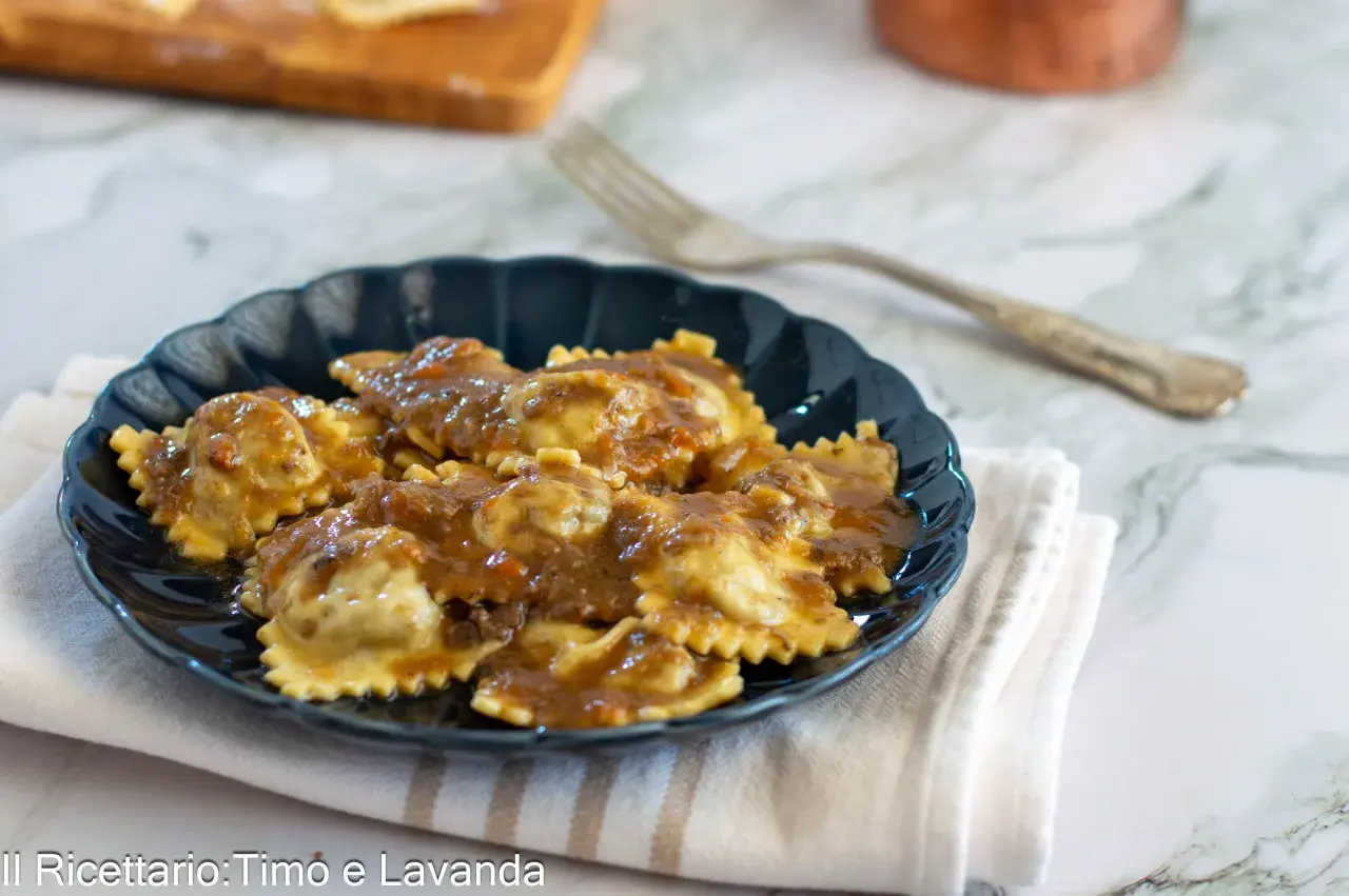Piatto di agnolotti al brasato, conditi con un sugo ricco e saporito, serviti su un piatto scuro.