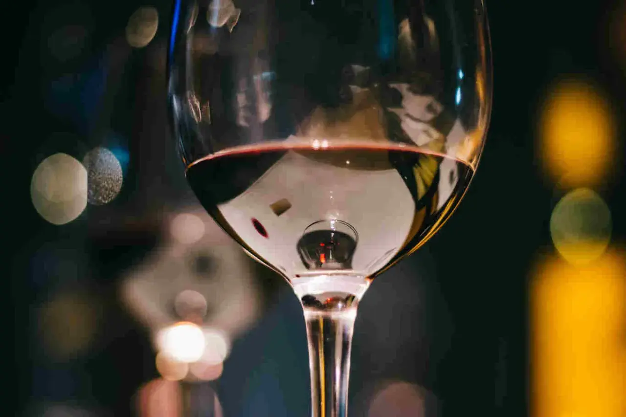 Un bicchiere di vino rosso riflette luci sfocate. Immagina tre bicchieri pronti per una degustazione serale.