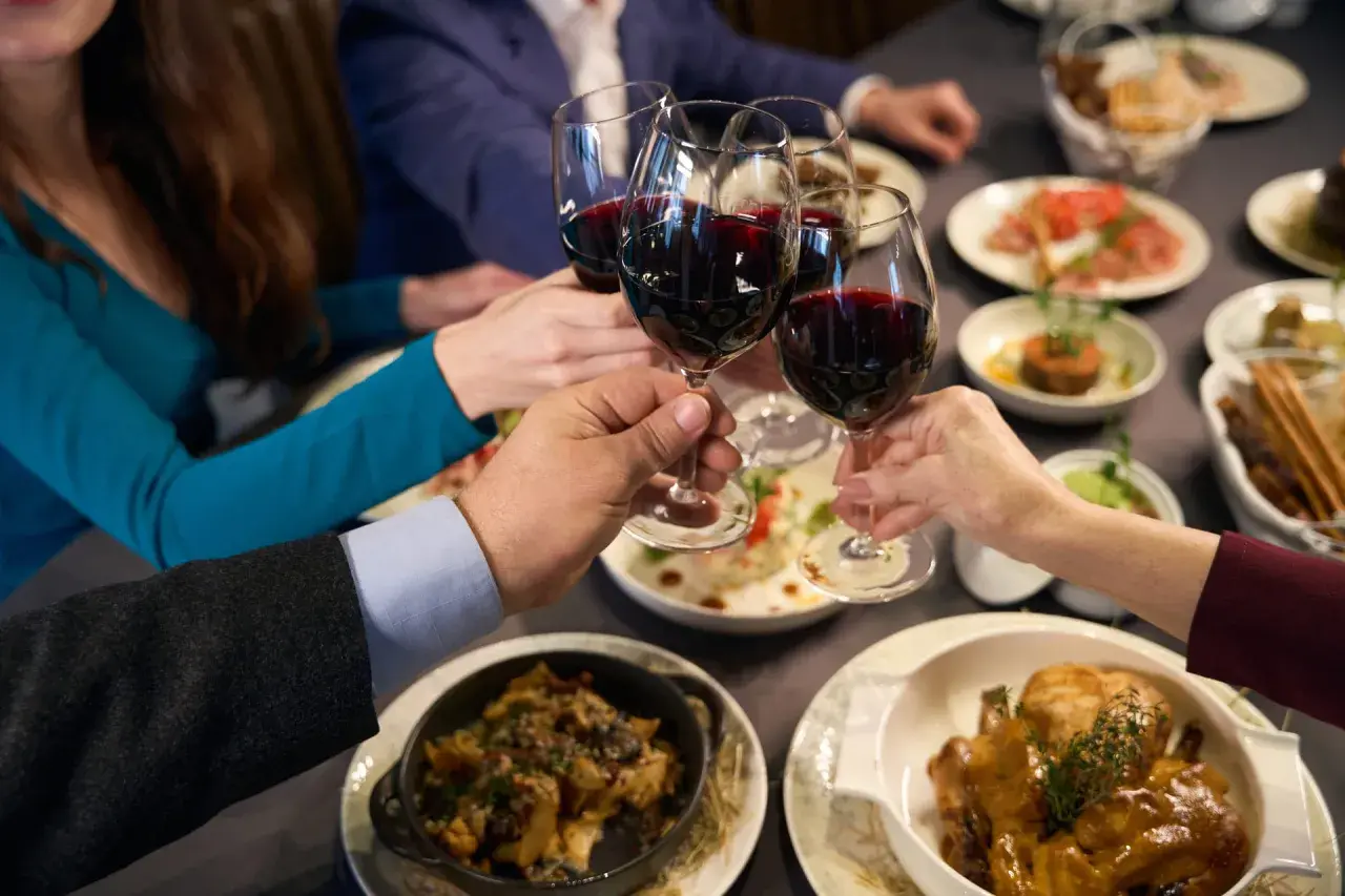 Brindisi con vino rosso, forse un Muller Thurgau, durante una cena conviviale con piatti invitanti.