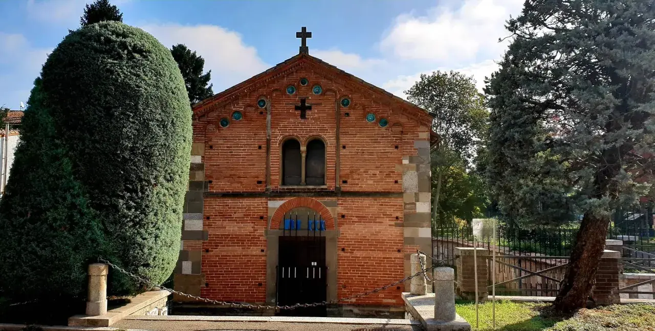 Chiesa in mattoni rossi con croce in cima, circondata da alberi verdi. Un luogo tranquillo, forse a Voghera dove si trova.