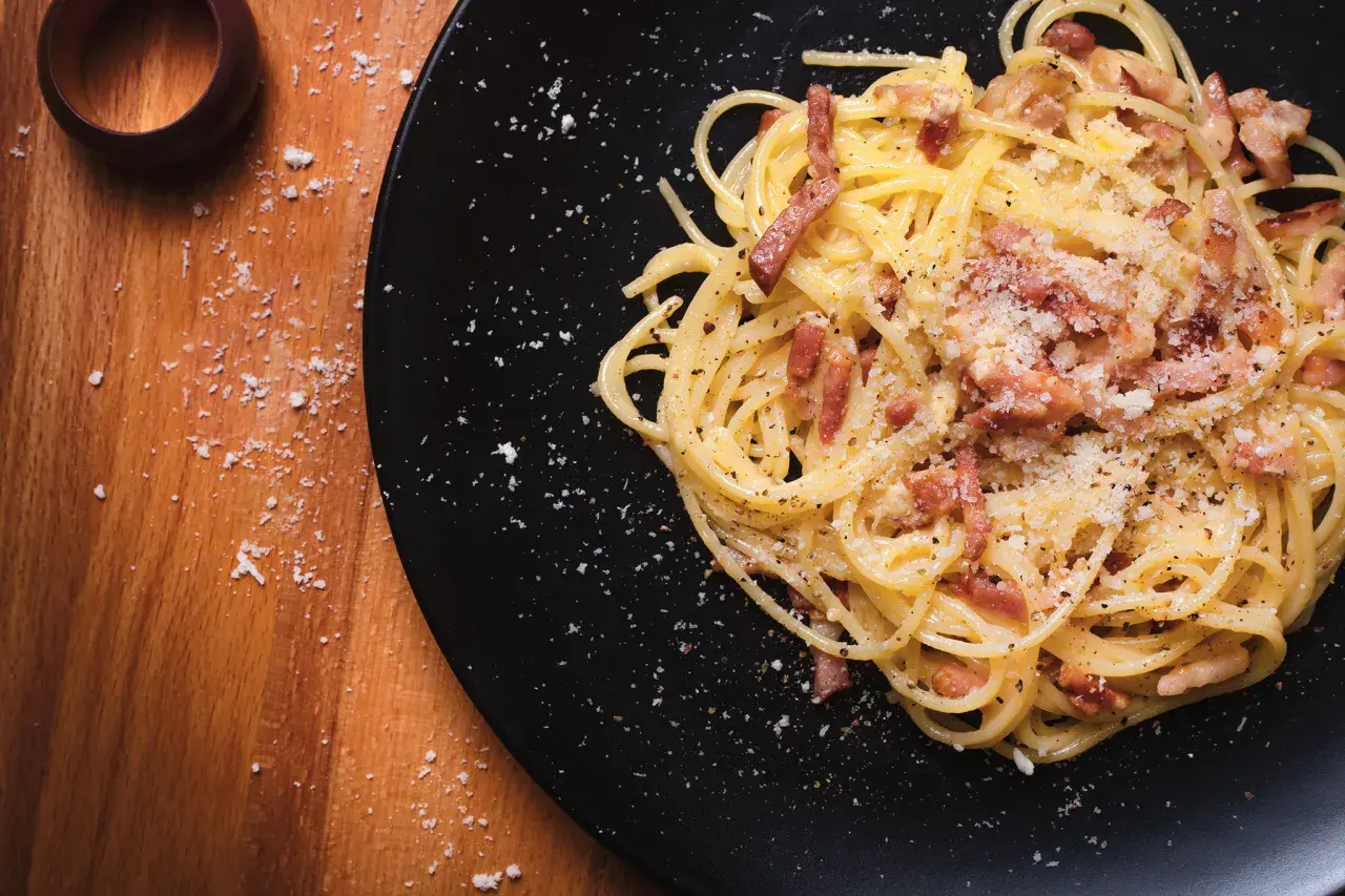 Spaghetti alla carbonara, un piatto che evoca la sua origine romana, con guanciale croccante e pecorino.