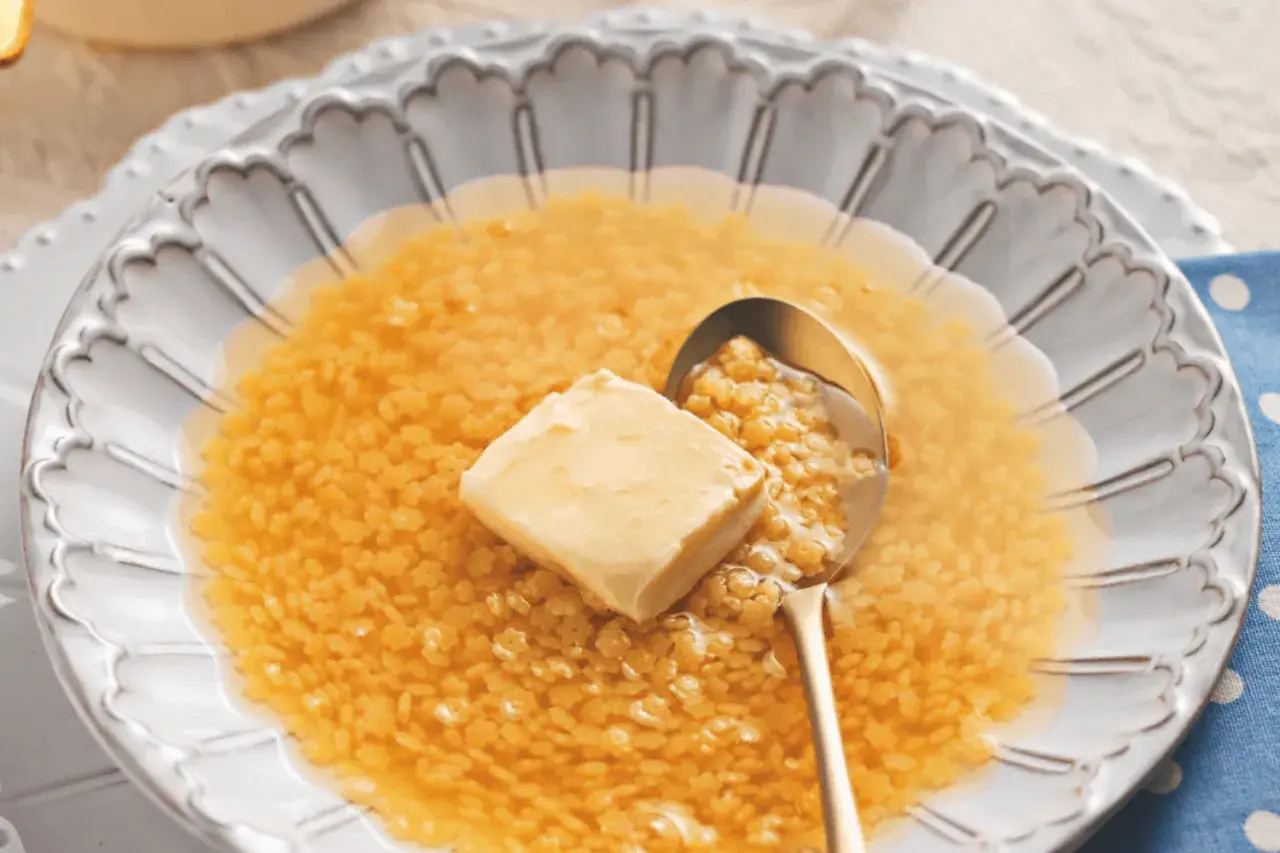 Minestrina in brodo con dado, un comfort food che scalda il cuore. Un cucchiaio d'oro raccoglie la pasta minuta e un cubetto di burro si scioglie nel brodo caldo.