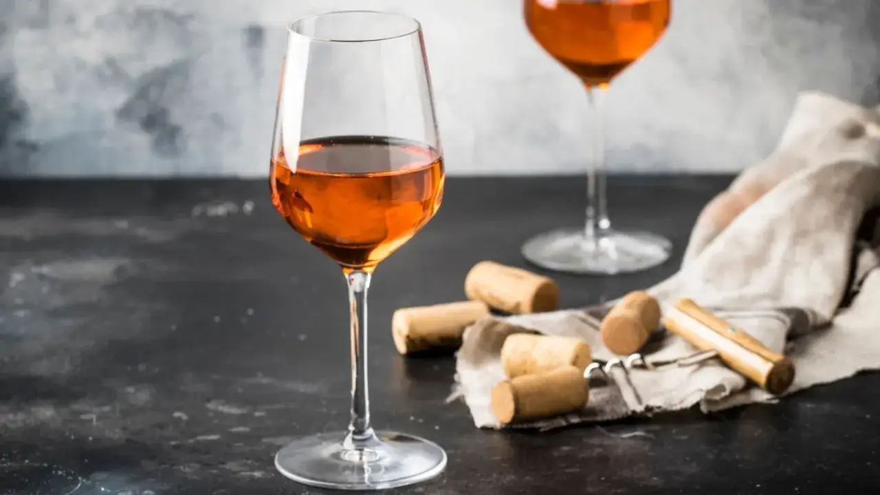 Calici di vino ambrato, su un tavolo scuro, con tappi di sughero e cavatappi. Un invito a gustare un vino da vendemmia tardiva.