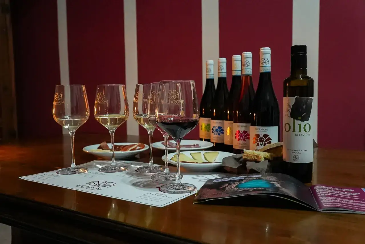 Calici di vino bianco e rosso, bottiglie e olio, con un assaggio di formaggio e salumi. Un invito a scoprire il trebbiano d'Abruzzo.