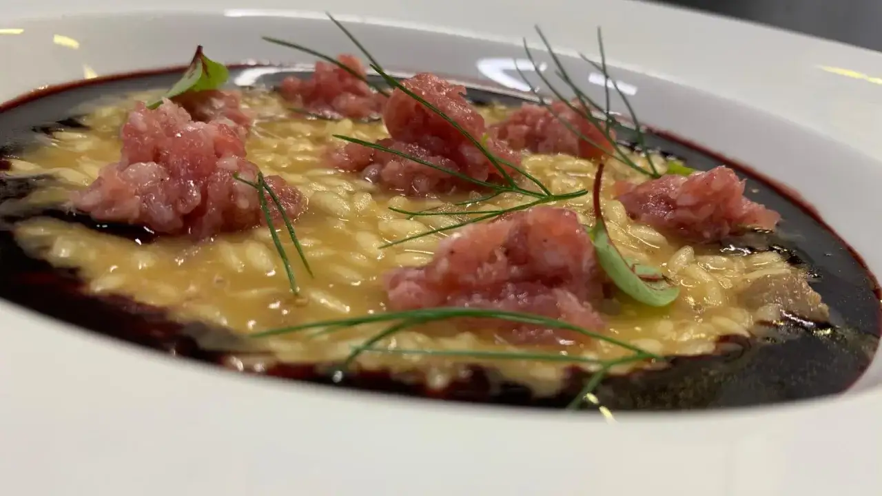 Risotto cremoso con pasta di salame, guarnito con erbe aromatiche e un filo di riduzione di vino rosso.