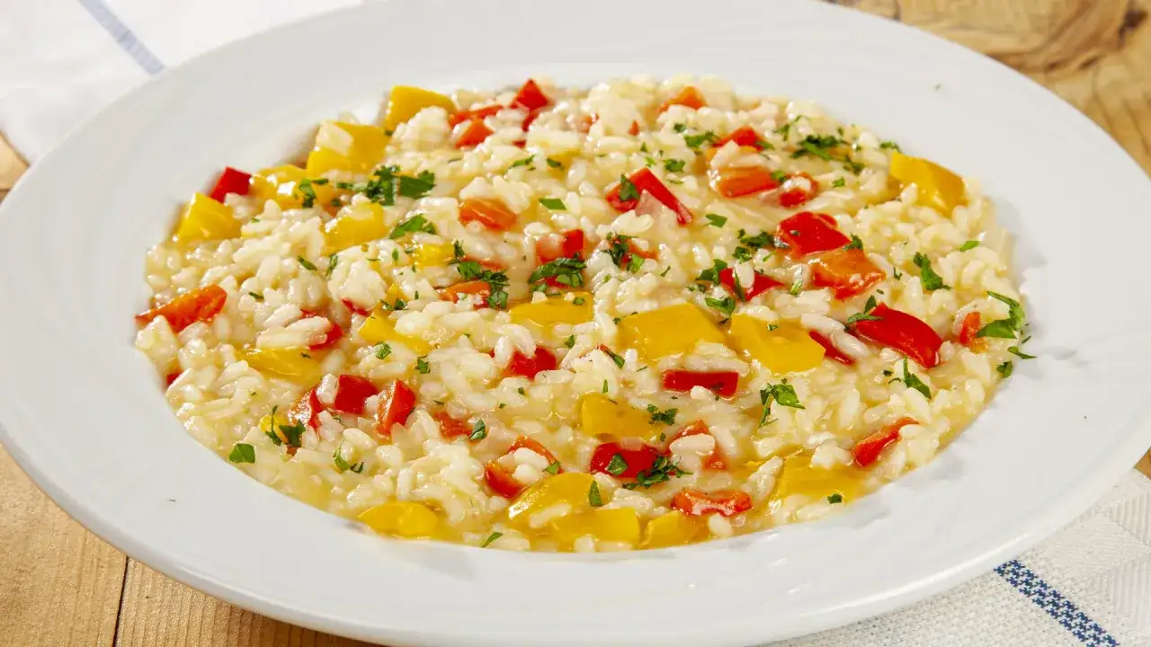Un cremoso risotto alla vogherese con peperoni rossi e gialli, guarnito con prezzemolo fresco.