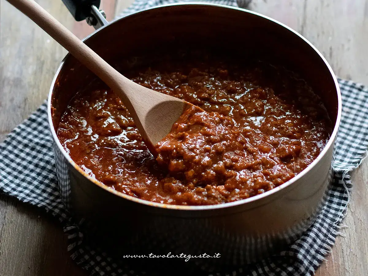 Sugo pronto per spaghetti bolognese, denso e saporito, in una pentola con mestolo di legno.
