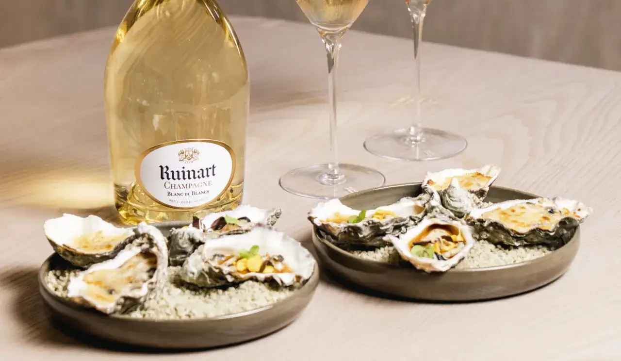 Ostriche fresche e dorate, accompagnate da una bottiglia di champagne Ruinart e calici scintillanti. Un'esperienza di lusso.