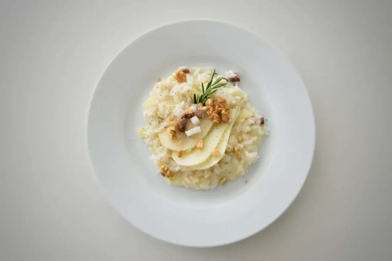 Risotto pere e taleggio cremoso, guarnito con noci croccanti, fettine di pera e rosmarino.