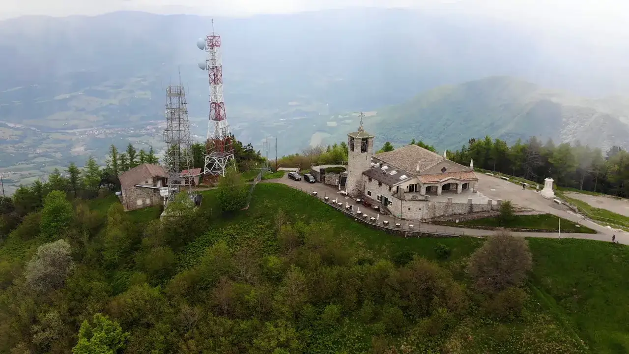 Edificio con campanile e antenne sul monte Penice, circondato da verde e nebbia.