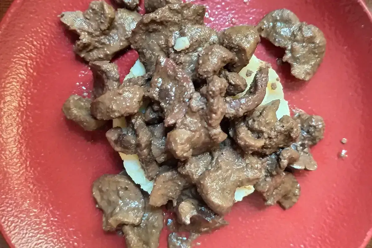 Un saporito piatto di frittura di maiale, con pezzi succulenti su una base bianca, servito su un piatto rosso.