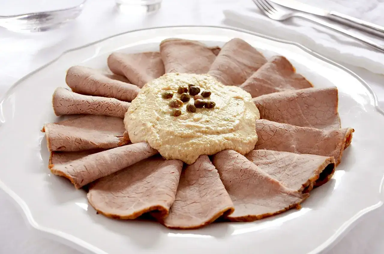 Vitello tonnato, un classico con origini piemontesi, servito su un piatto bianco con salsa cremosa e capperi.