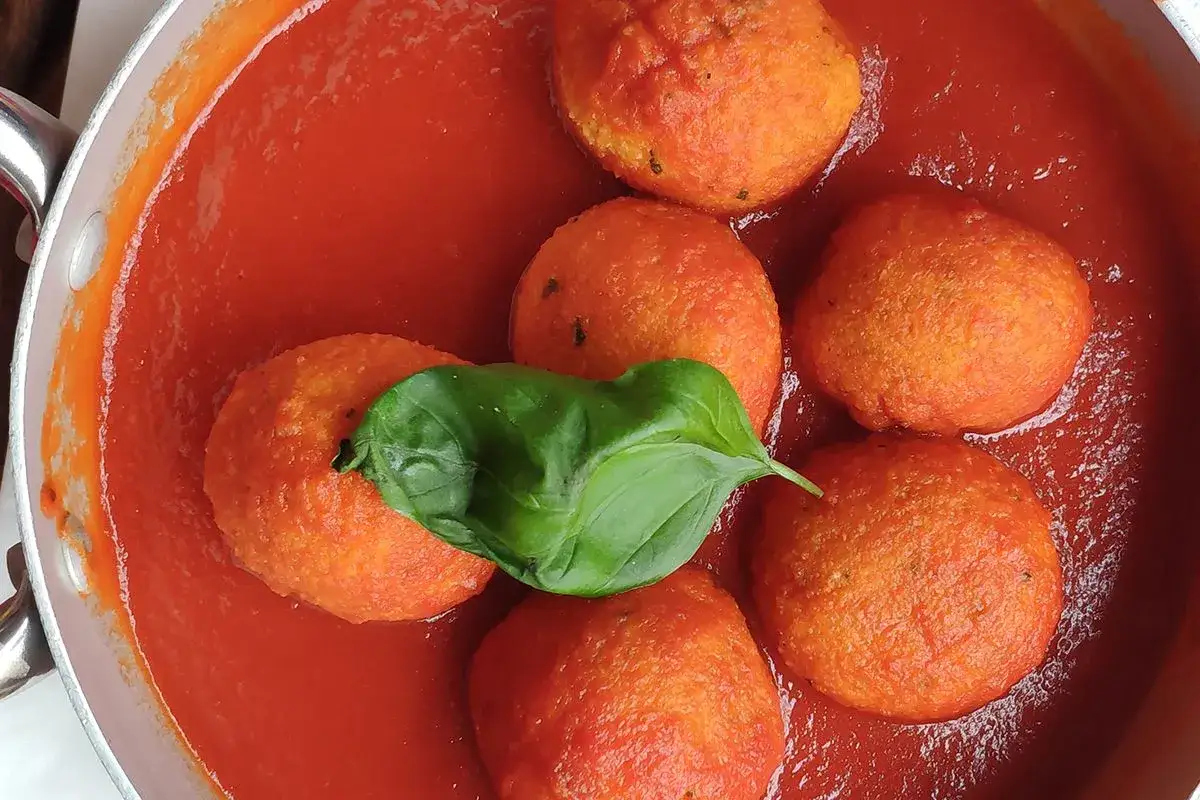 Pallotte cacio e ova in un sugo rosso brillante, guarnite con una foglia di basilico fresco.