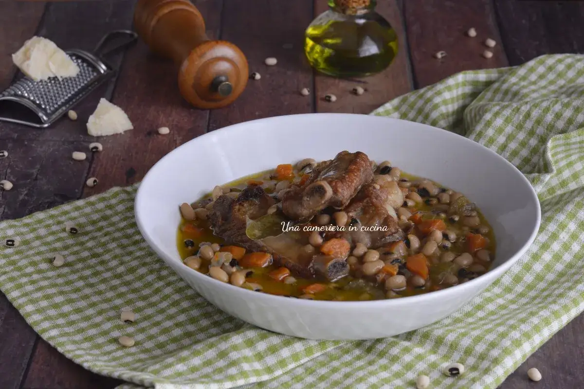 Una ciotola di zuppa dei morti con fagioli, costine di maiale e carote, su un tovagliolo a quadri verdi.