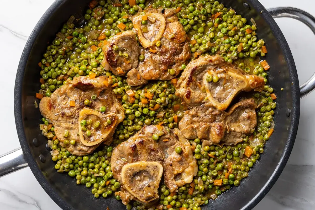 Ossobuco ricetta con piselli in padella, un piatto succulento e colorato, pronto per essere gustato.