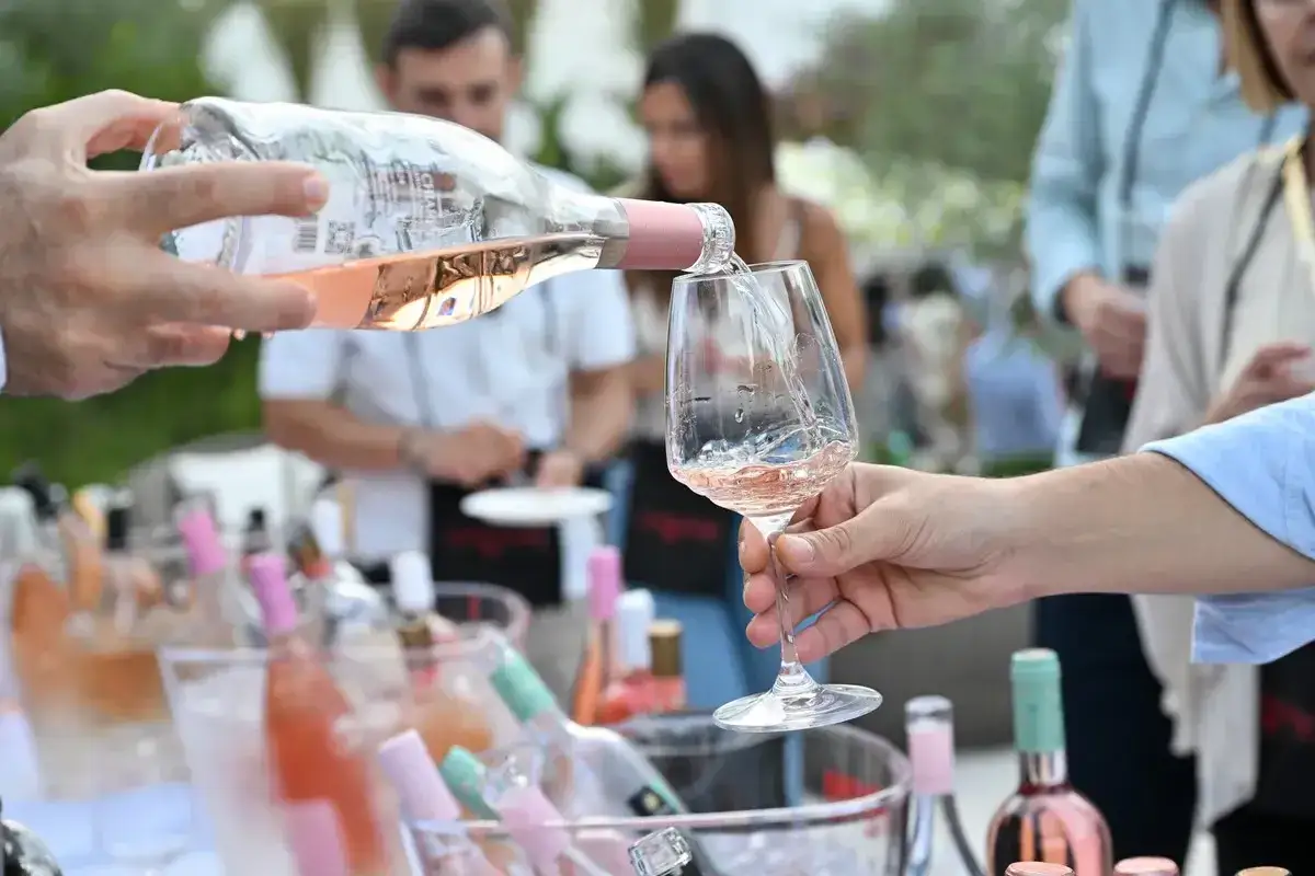 Versando il miglior vino rosato italiano in un bicchiere, con bottiglie in fresco sullo sfondo.