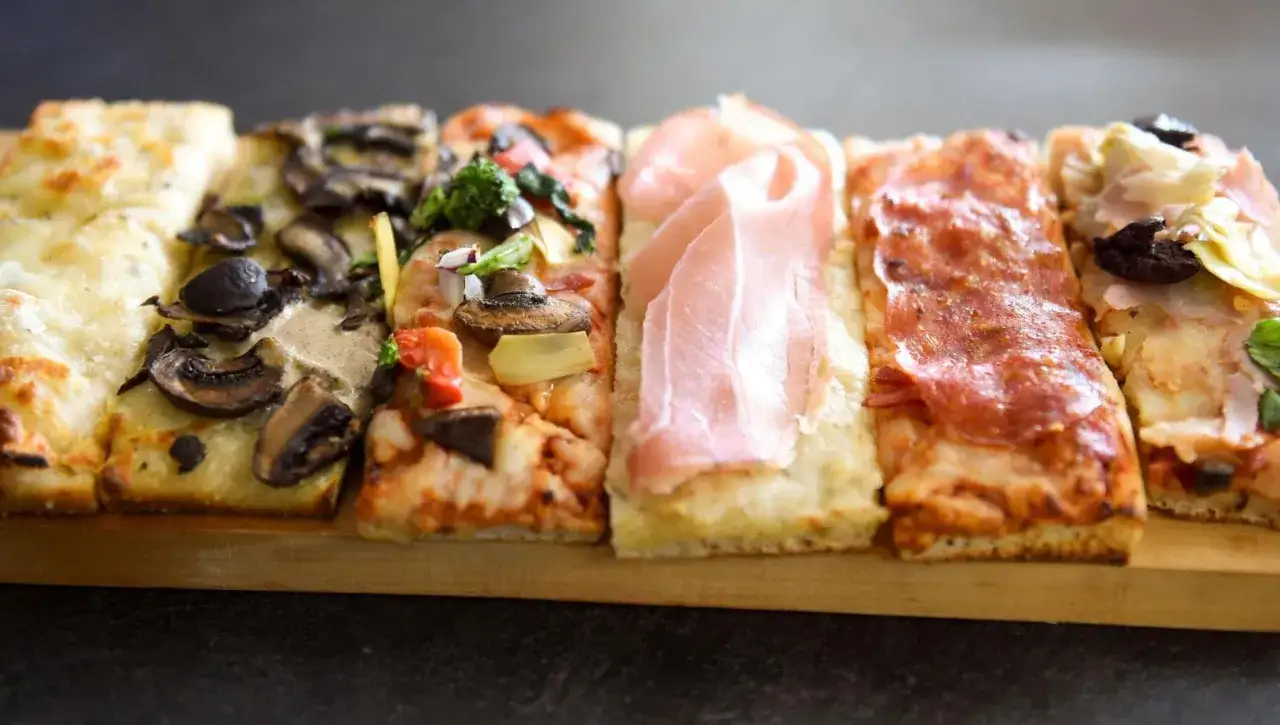 Una selezione di gustose fette di pizza al taglio: funghi, prosciutto, salame e verdure.