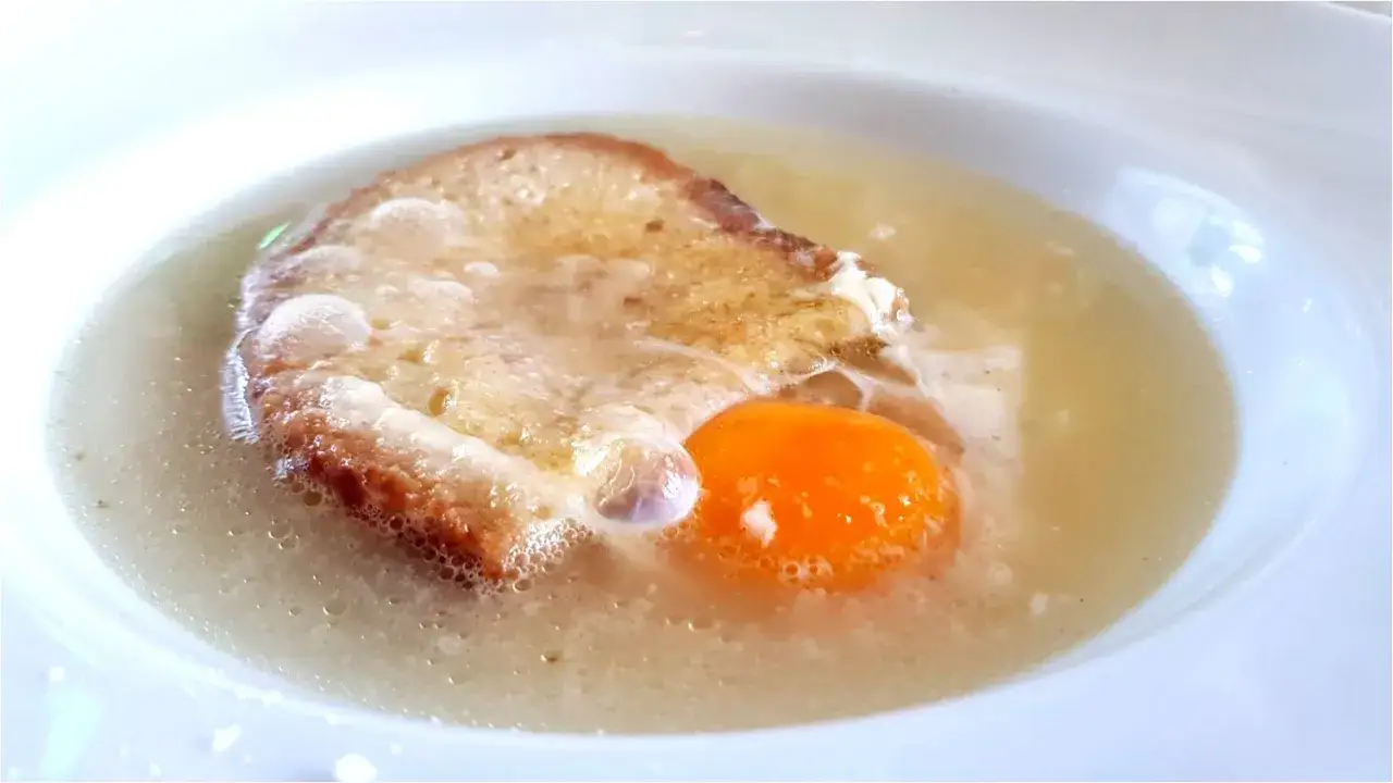 Un uovo in brodo con pane tostato, un piatto tipico di Pavia, servito in una ciotola bianca.