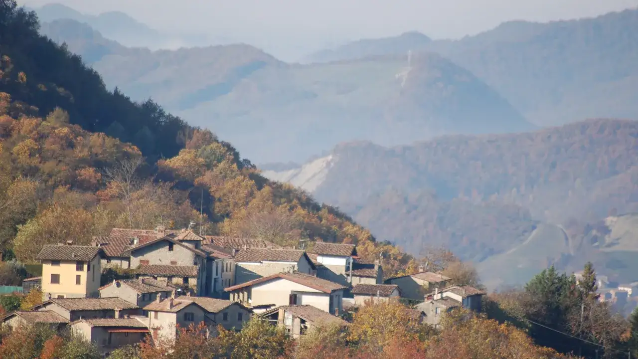 Borgo tra le colline autunnali, con case in pietra e tetti rossi. Un invito a percorrere il sentiero delle fontane, tra i colori caldi della natura.