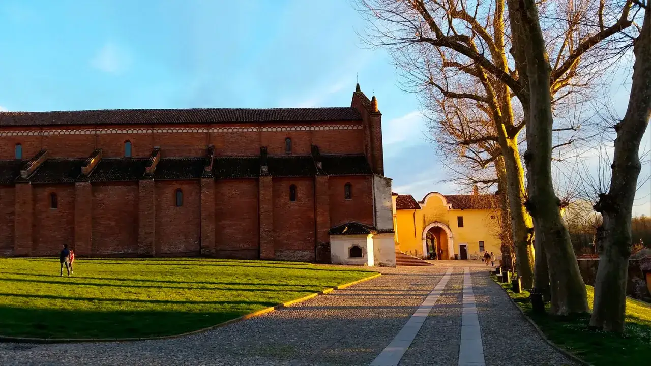 Morimondo cosa vedere: imponente abbazia in mattoni rossi, viale alberato e cielo azzurro.