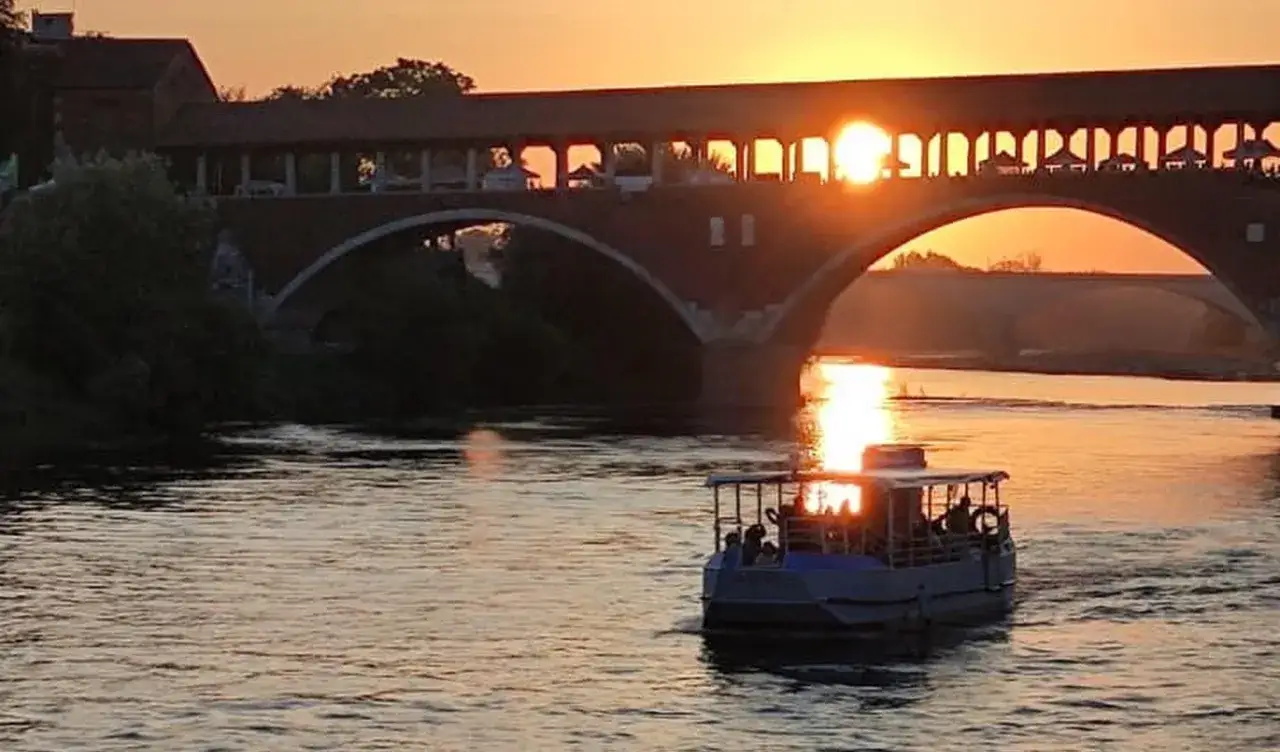 Tramonto dorato sul fiume, con un battello che naviga sotto un suggestivo ponte coperto.