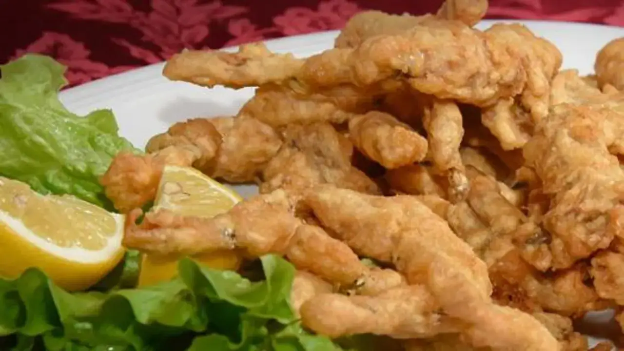 Un piatto invitante di rane fritte croccanti, servite con spicchi di limone fresco e foglie di lattuga verde.